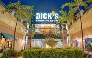 Dick's Sporting Goods storefront at dusk with lit sign, palm trees, and neighboring shops at Gulf Coast Town Center