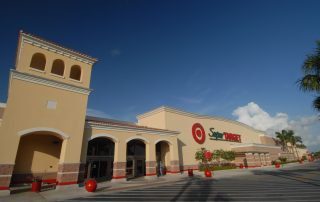 Completed SuperTarget store with tan stucco facade, arched entry, tile-roofed tower, and palm trees at Gulf Coast Town Center