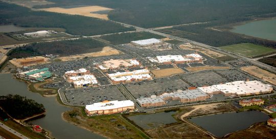 Aerial view of Gulf Coast Town Center, a large open-air shopping center with parking lots, ponds, a highway and surrounding