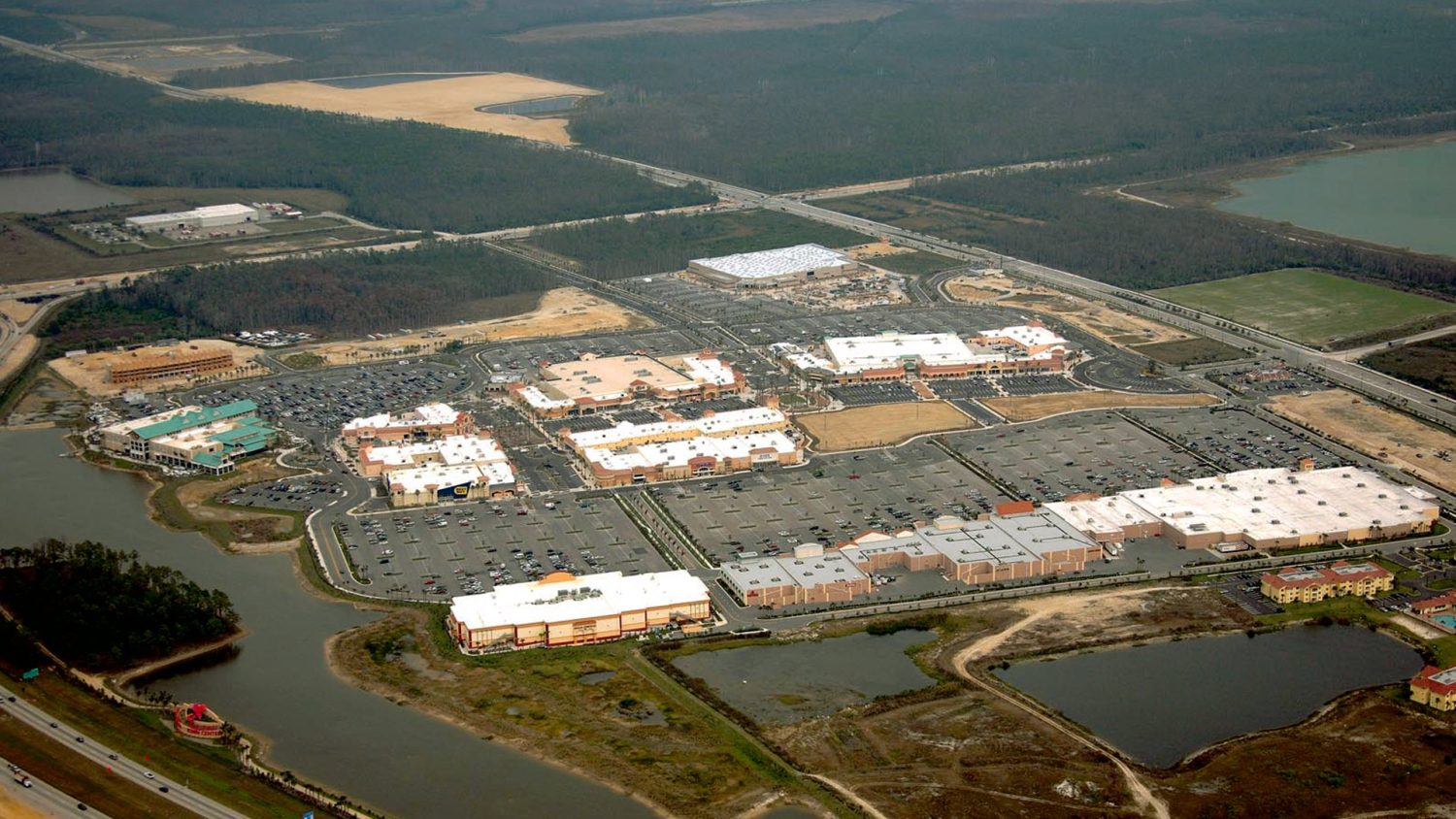 Aerial view of Gulf Coast Town Center, a large open-air shopping center with parking lots, ponds, a highway and surrounding