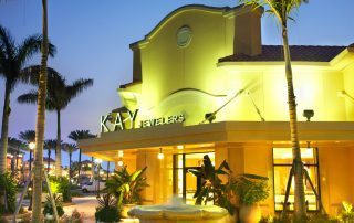 Kay Jewelers storefront at Gulf Coast Town Center at dusk, with a tiered fountain, palm trees, and a tile roof