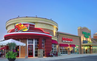 Red Robin restaurant with curved red tower facade beside a Dollar Tree in a lit brick retail strip at dusk, Gulf Coast Town