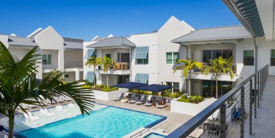 The Mark Luxury Condominiums courtyard pool with lounge chairs, palm trees, and white buildings with metal roofs, seen from