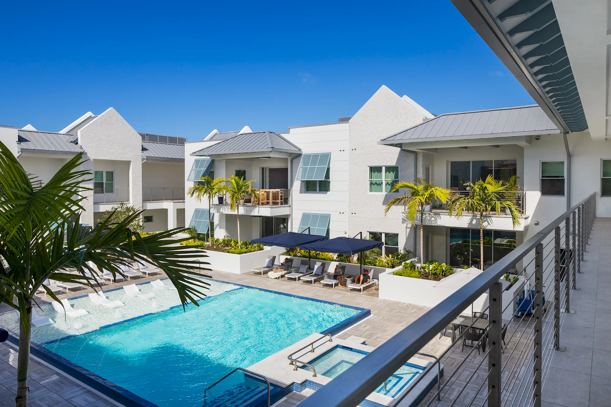 The Mark Luxury Condominiums courtyard pool with lounge chairs, palm trees, and white buildings with metal roofs, seen from
