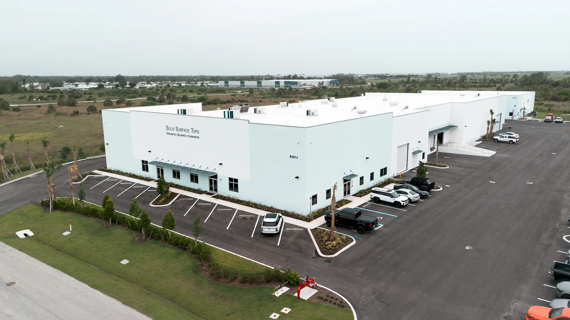 Aerial view of a white Solid Surface Tops manufacturing facility with a landscaped parking lot and loading doors