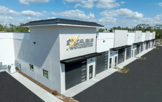 Aerial view of Excalibur Motor Condominiums, a new white building with a row of dark garage doors and metal awnings beside