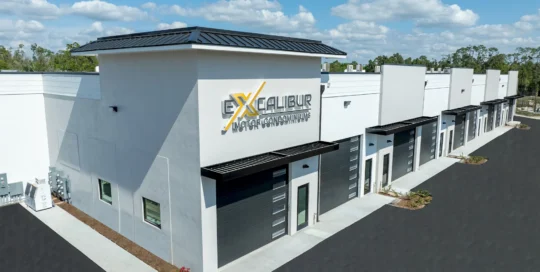 Aerial view of Excalibur Motor Condominiums, a new white building with a row of dark garage doors and metal awnings beside