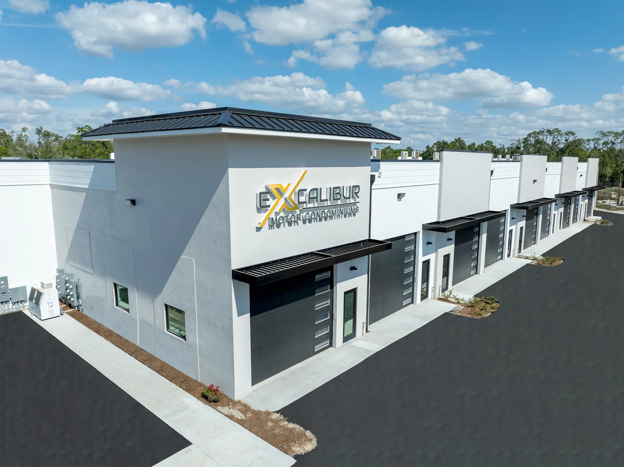 Aerial view of Excalibur Motor Condominiums, a new white building with a row of dark garage doors and metal awnings beside