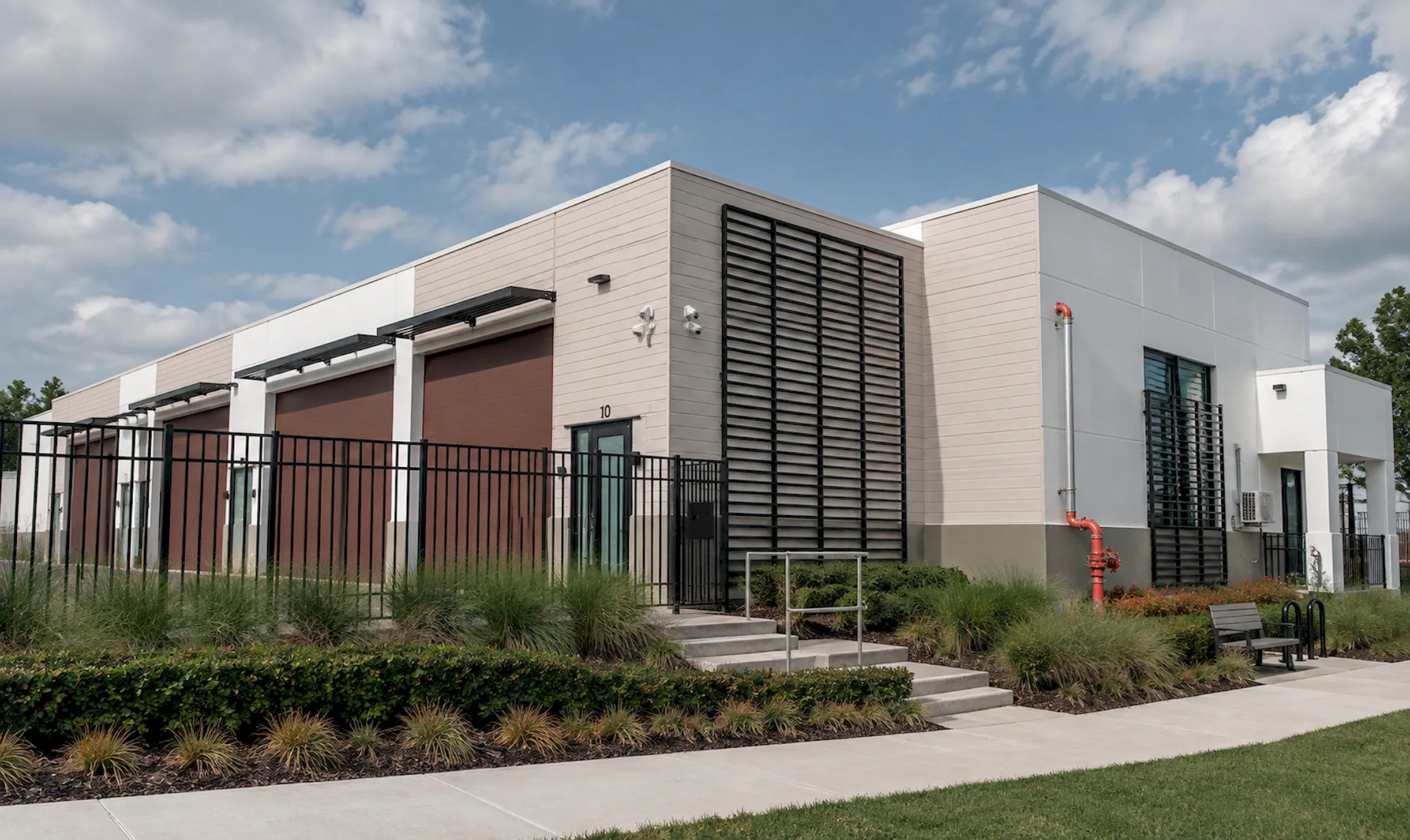 Completed Pine Street storage warehouse with brown roll-up doors, black louvered panels, fencing, and landscaped walkway