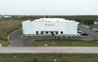 Aerial view of white Solid Surface Tops facility, signed Granite, Quartz, Cabinets, with new parking lot and young palm
