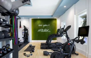 Fitness center at The Mark Luxury Condominiums with neon "on your MARK" sign on a green wall, treadmills, bikes and weights