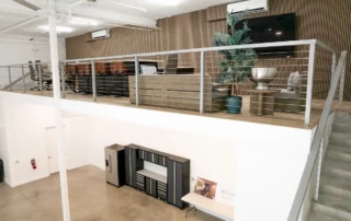 Finished mezzanine lounge with cable railing and wood slat wall above garage space with cabinets at Excalibur Car