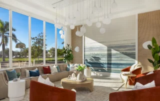 Lounge at The Mark with floor-to-ceiling windows, curved sectional, rust armchairs, globe pendant cluster and ocean mural