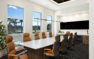 Conference room with marble table, tan high-back chairs, wall display, wet bar and windows facing palm trees in GCM's office