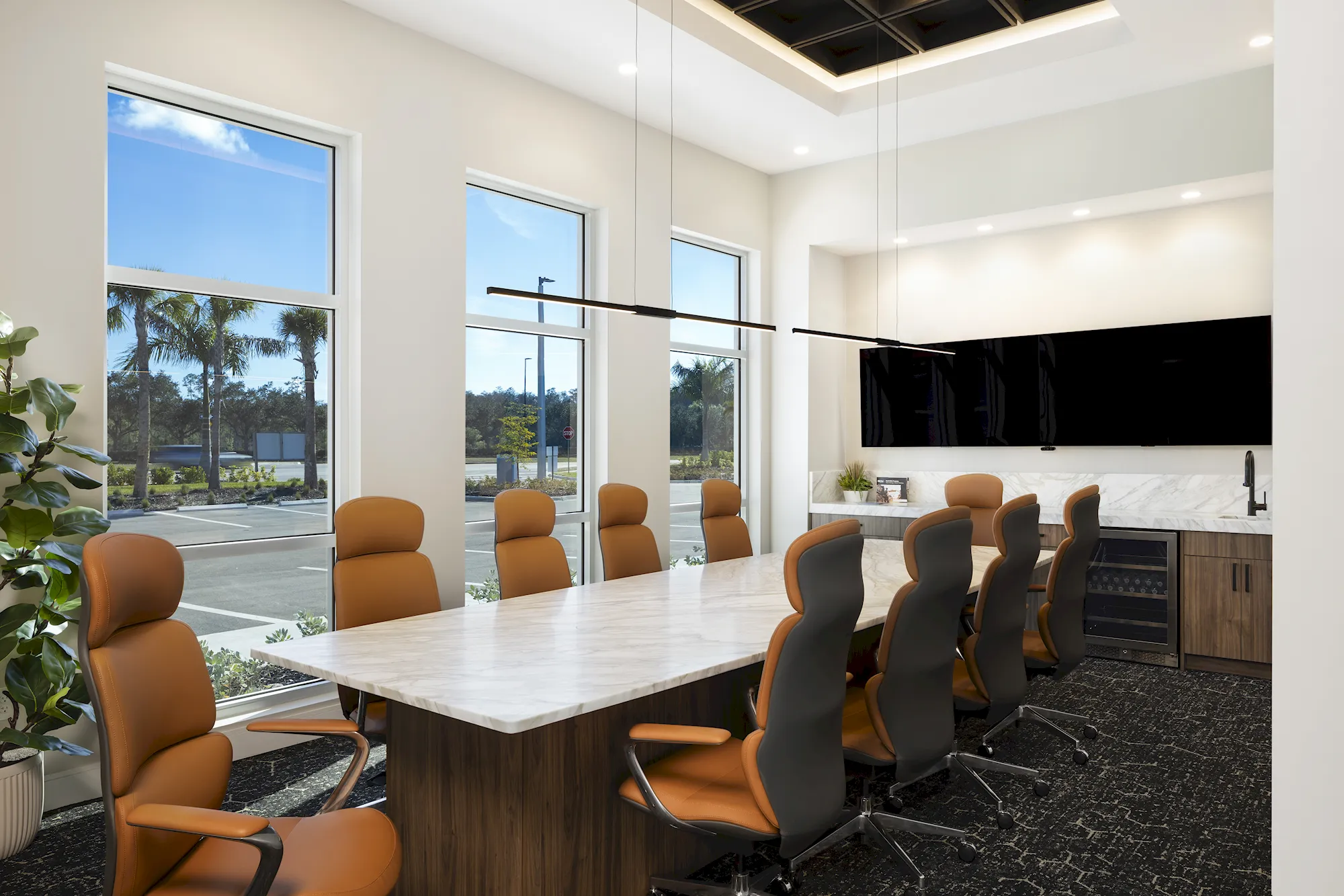 Conference room with marble table, tan high-back chairs, wall display, wet bar and windows facing palm trees in GCM's office