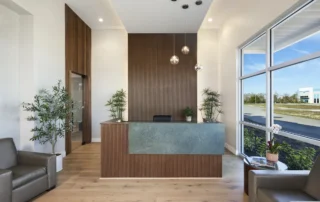 Lobby of GCM Contracting office with green stone reception desk, wood accent wall, pendant lights, and tall windows