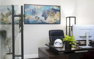 Private office with a white GCM hard hat on a dark wood desk, world map artwork, and a glass door with black pull handle