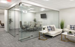 Glass-walled Conference Room 2 with table and chairs beside a lounge with white leather sofas in a finished office interior